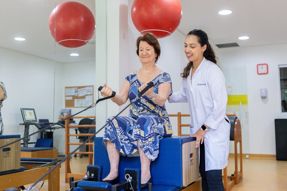 Funcionária ajudando senhora em exercício no pilates